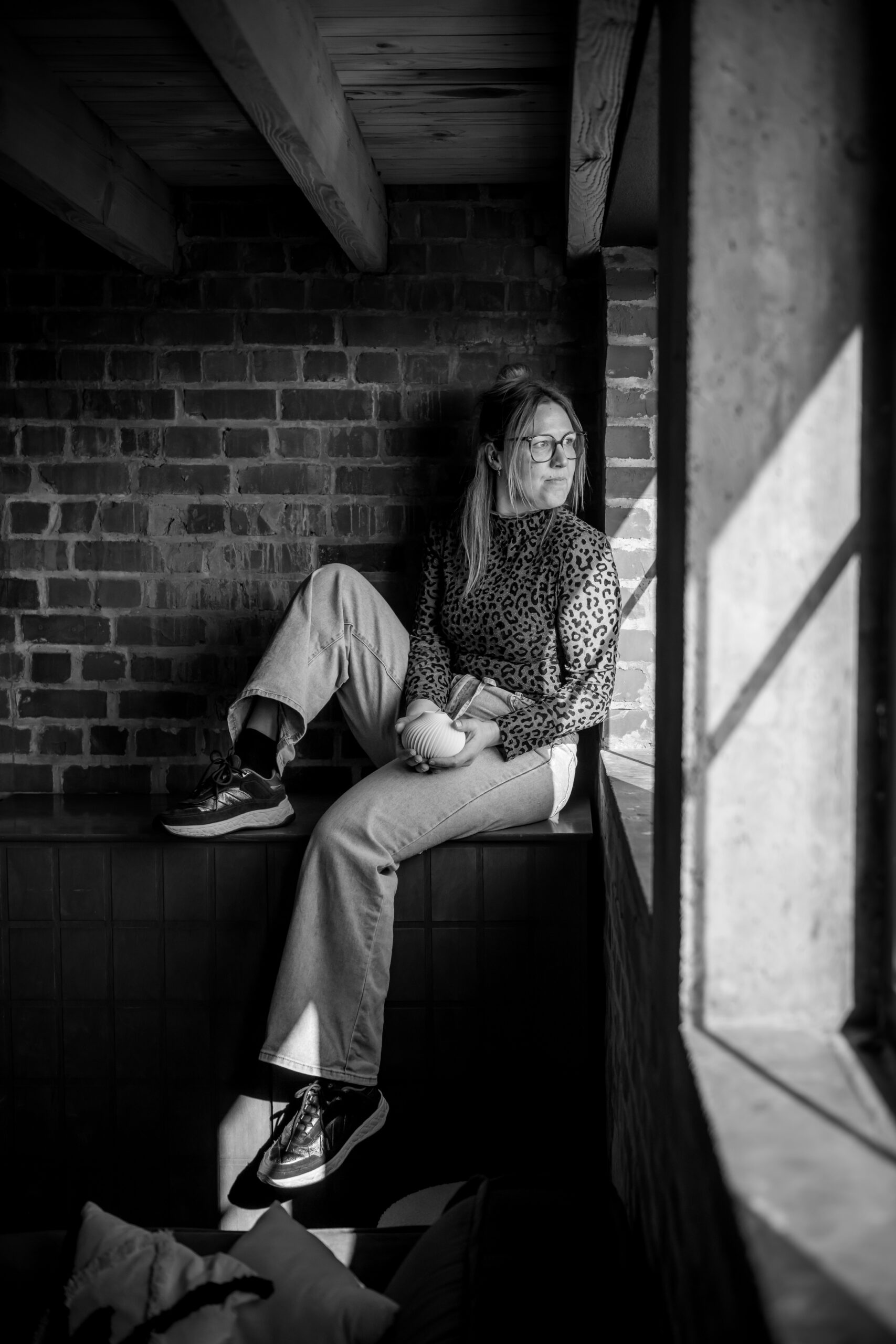 Zwart-witfoto van een vrouw aan het raam — reflectief, stijlvol en met natuurlijke schaduwval